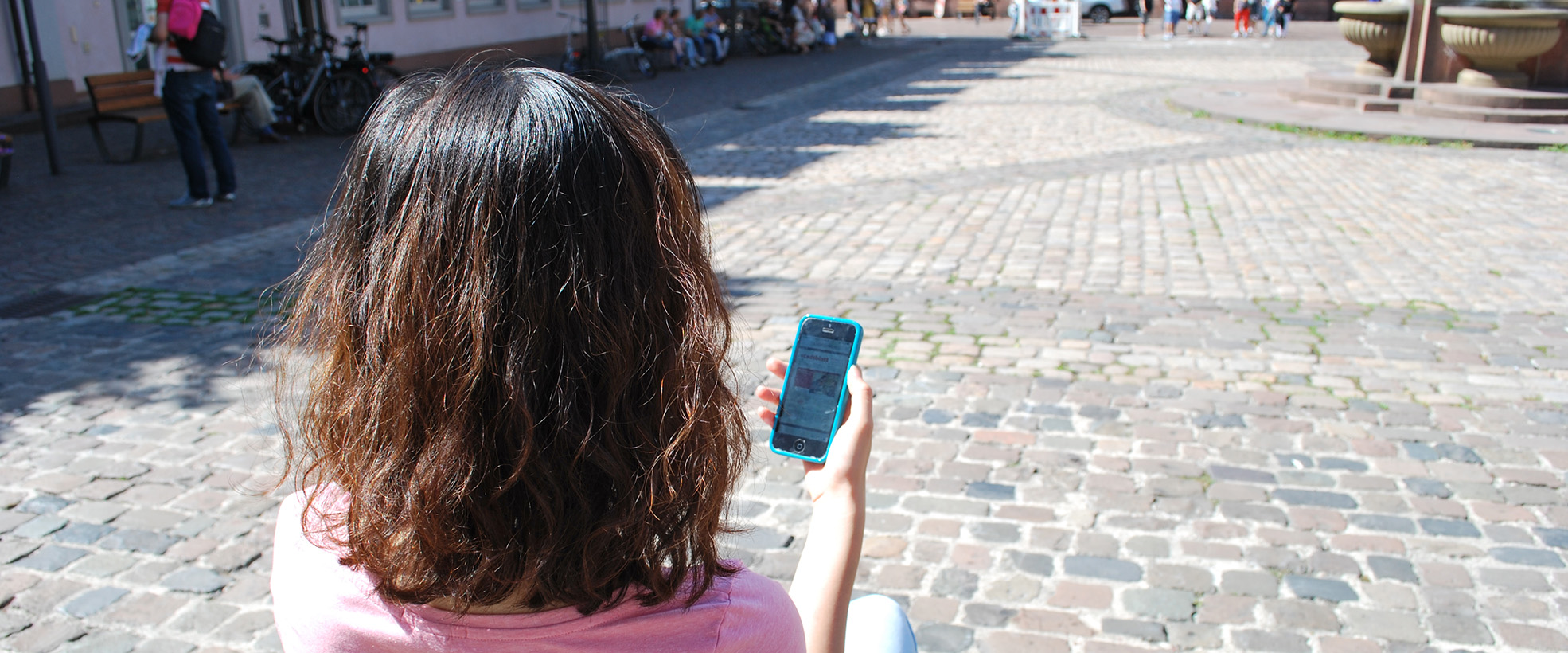 Blick von hinten auf eine junge Frau, die auf ihr Smartphone schaut.
