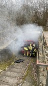 zwei Feuerwehrmänner arbeiten an einem rauchenden PKW