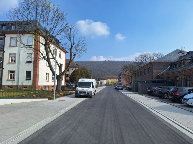Fertig gestellt: die Adelheid-Steinmann-Straße in der Südstadt. Sie liegt nahe am Paradeplatz. (Foto: Stadt Heidelberg) Neue Straße, am Rnd parken Autos. Neben der Straße steht ein großes Haus.