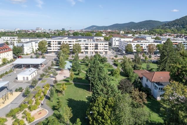 In der neuen Südstadt sind bereits 2.800 Menschen zu Hause. Von 2018 bis 2025 entstanden rund 1.100 Wohnungen im Neubau und im Bestand. „Der Andere Park“ (Mitte) ist das grüne Herz des Quartiers. Dazu gehört der Checkpoint (links), der an die frühere militärische Nutzung erinnert. (Foto: Christian Buck) Foto von einer Stadt aus der Vogelperspektive.