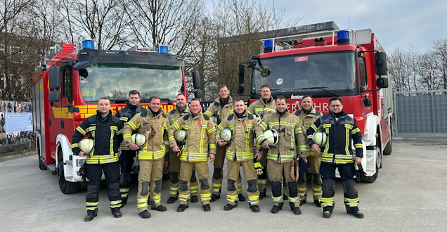 Gruppenbild der Lehrgangsteilnehmer mit Einsatzkleidung, die vor zwei Feuerwehrfahrzeugen stehem