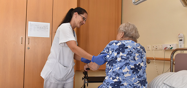 Pflegerin hilft Seniorin beim Aufstehen.